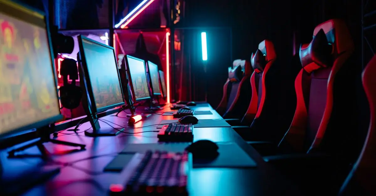 Rows of gaming PCs and chairs under neon light